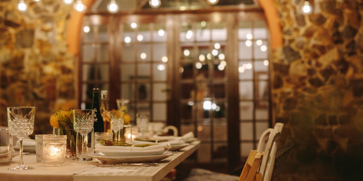 Elegant outdoor dinner table set with plates, glasses, and candles under string lights on a stone patio