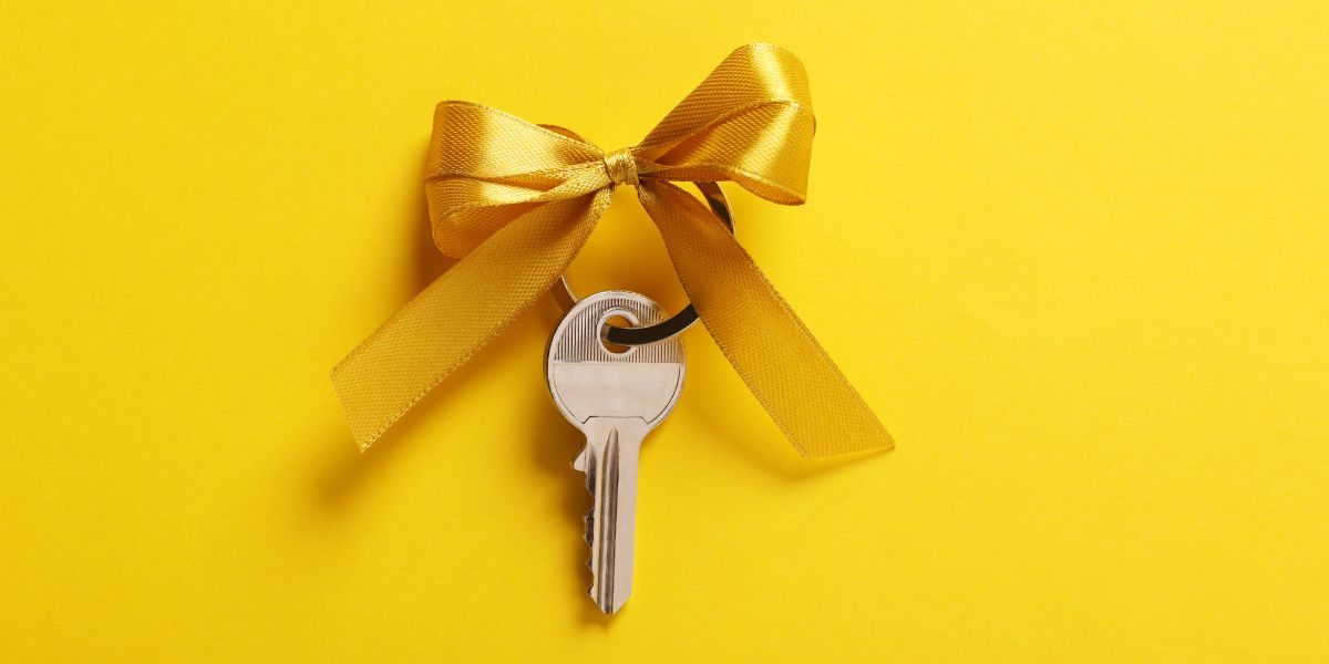 Silver key tied with a gold ribbon against a bright yellow background.