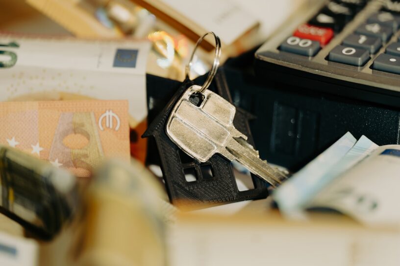 Person's hands at a clean, modern desk using a calculator next to a set of house keys, symbolizing the calculation of home...
